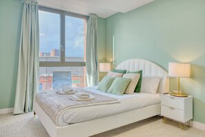 A neatly made bed with pillows, a bedside lamp, and a window with curtains.