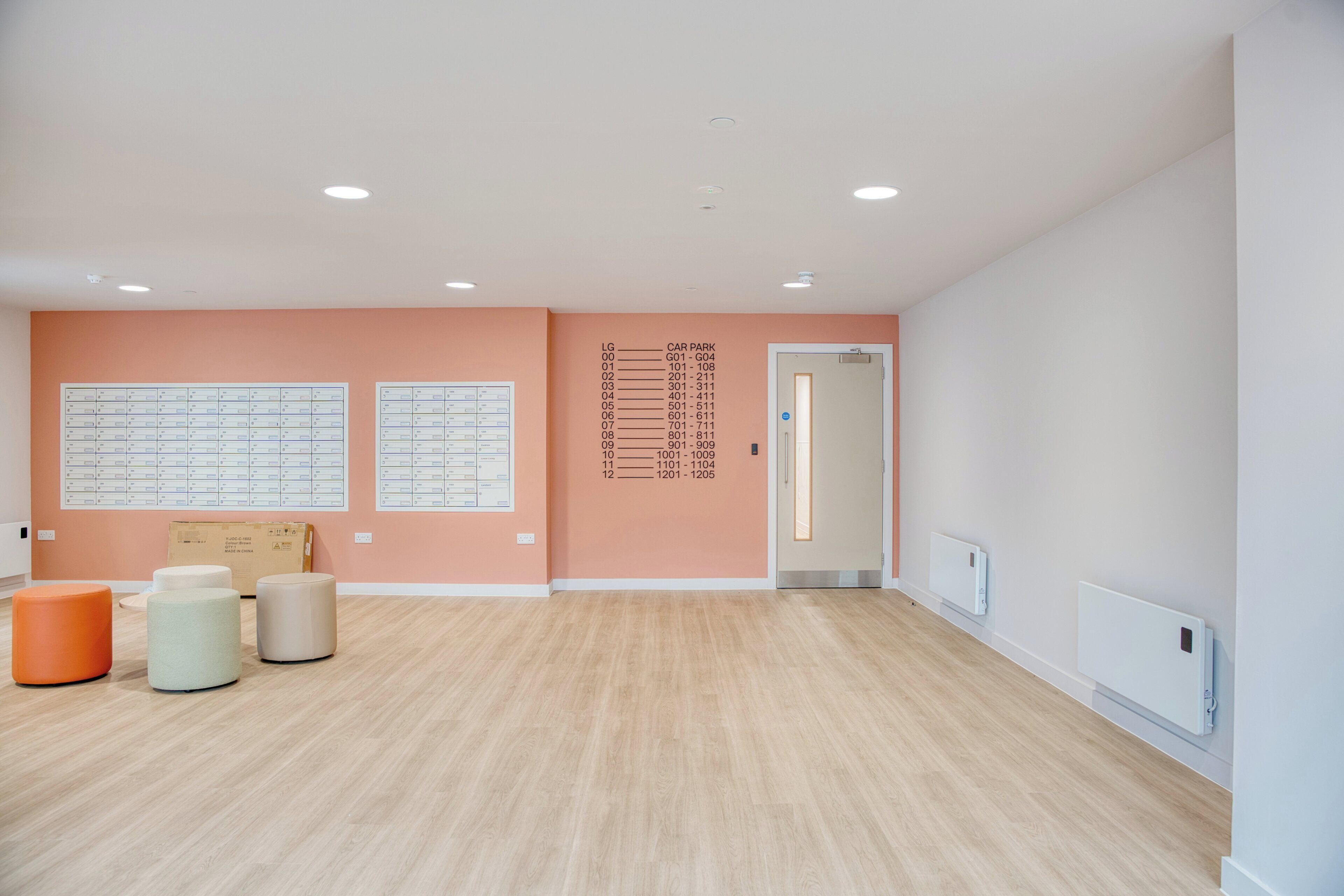 A spacious room with a wooden floor, a wall with a car park sign, and three cylindrical stools.