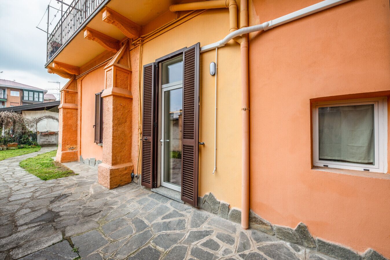 A building with a stone-paved entrance, a balcony with metal railings, and a window with a white frame.