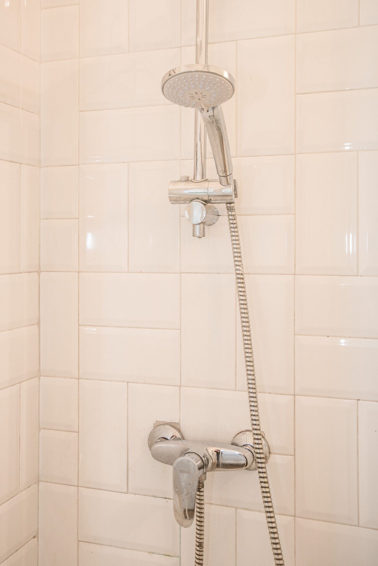A shower with a handheld showerhead and a wall-mounted faucet.