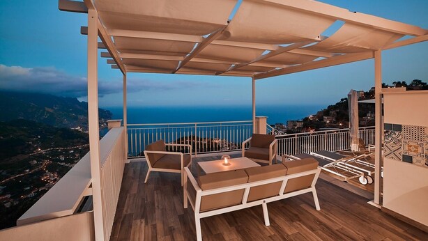 Ein Balkon mit Holzboden, weißen Möbeln und Blick aufs Meer.