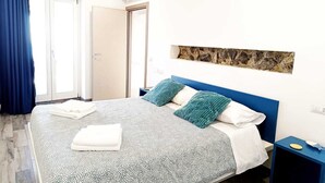 Ein Schlafzimmer mit Bett, Nachttisch, Wand-Klimaanlage, einer Tür und einem Fenster mit Vorhängen.