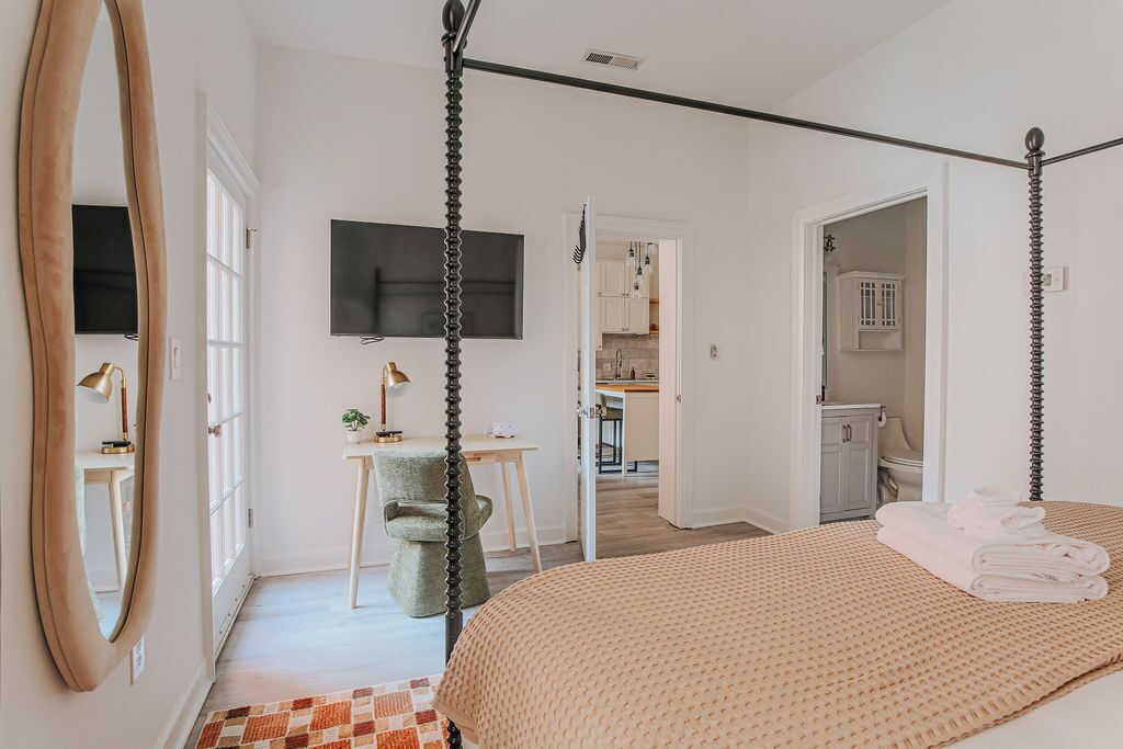 Een slaapkamer met een hemelbed, een grote spiegel, een flatscreen-televisie en uitzicht op de keuken.