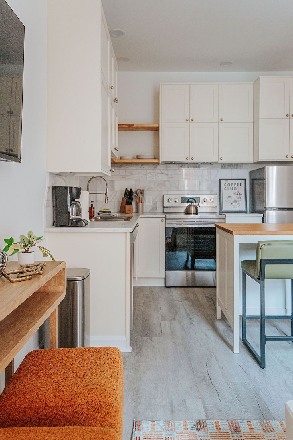 Een moderne keuken met witte kasten, roestvrijstalen apparatuur, een kunstwerk met koffie thema en een houten bankje.