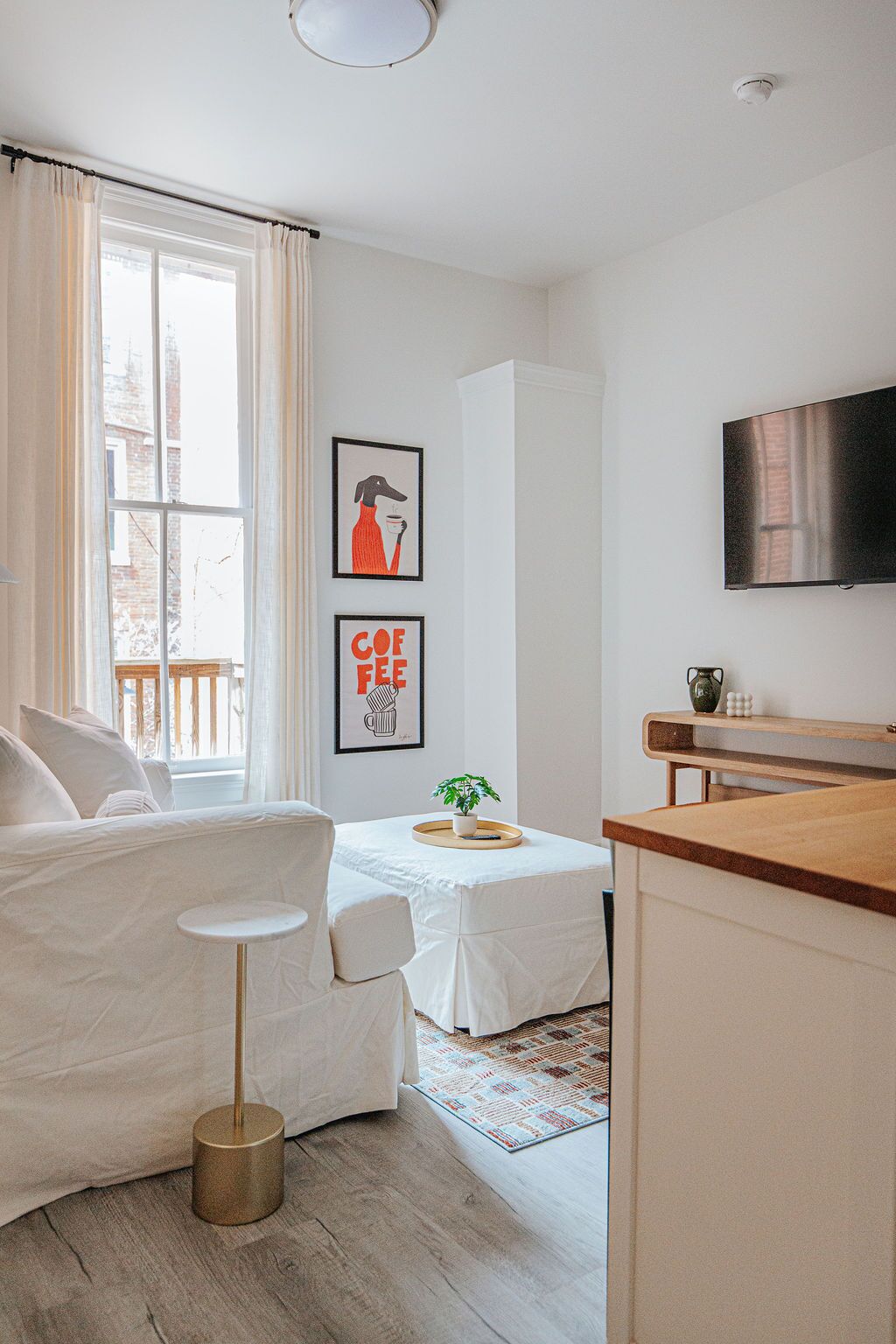 Een moderne, minimalistische woonkamer met een bank, een bijzettafeltje, een salontafel, een televisie en een raam met gordijnen.