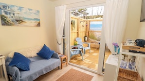 A cozy room with a sofa, a small table, and a view of the beach through a glass door.