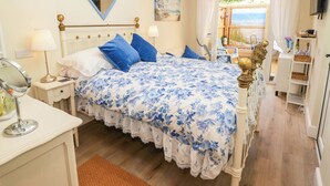 A bedroom with a bed, a nightstand, a dresser, a mirror, and a view of the outdoors.