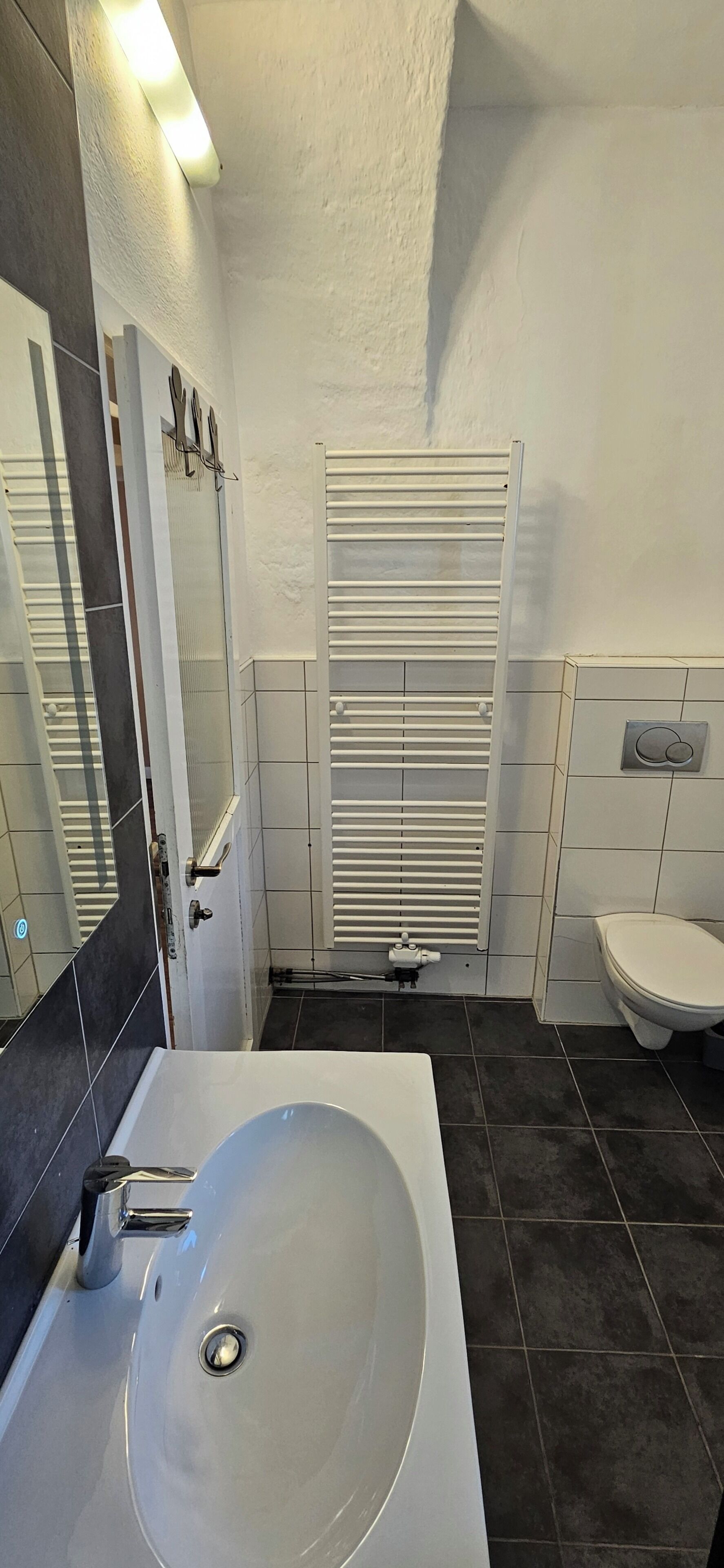 Ein Badezimmer mit Waschbecken, Spiegel, Handtuchhalter, Toilette und Heizkörper.
