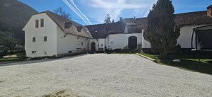 Ein Gebäude mit einem Schotterweg, einem großen Baum und einem Berg im Hintergrund.