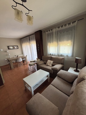 Un salon comprenant un canapé, une table basse, une table à manger avec des chaises et une fenêtre avec des rideaux.
