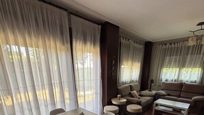 Un comedor con mesa y sillas de madera, un conjunto de sofá y vistas amplias a través de ventanas con cortinas.