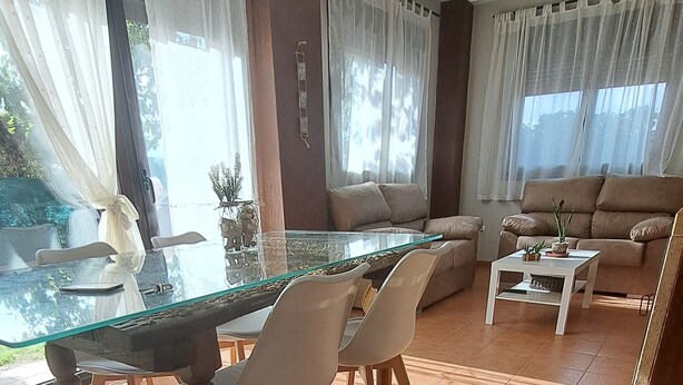 Una sala de estar con una mesa de comedor de vidrio, sillas blancas, un sofá y una mesa de centro.