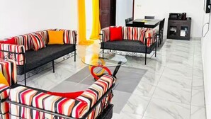 A modern living room with striped sofas, a glass coffee table, and a dining area with a dark cabinet. - Résidence au 2 Plateaux 3 Chambres (Abidjan)