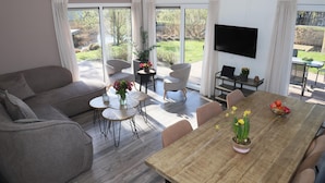 A modern living room with a sofa, dining table, chairs, a TV, and large windows. - Chalet in Biddinghuizen, Pool Facilities (Biddinghuizen)