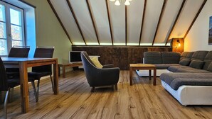 A cozy room with a wooden floor, a sofa, a chair, a small table, and a desk with a laptop.