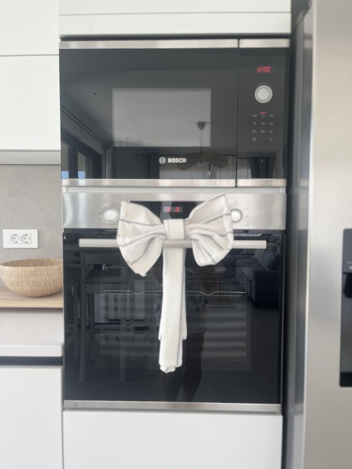 Une cuisine équipée d’un four Bosch, une serviette blanche nouée en forme de ruban, et un saladier en bois posé sur le plan de travail.