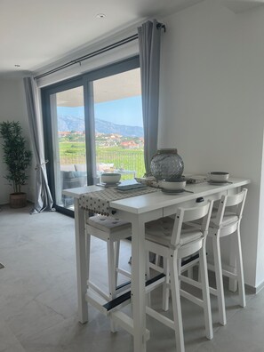 Ein Essbereich mit Tisch für zwei Personen, einer Topfpflanze und Blick auf eine gebirgige Landschaft durch große Fenster.