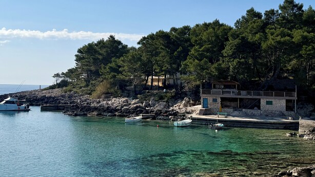 A coastal scene with clear water, boats, and a stone building with a balcony.