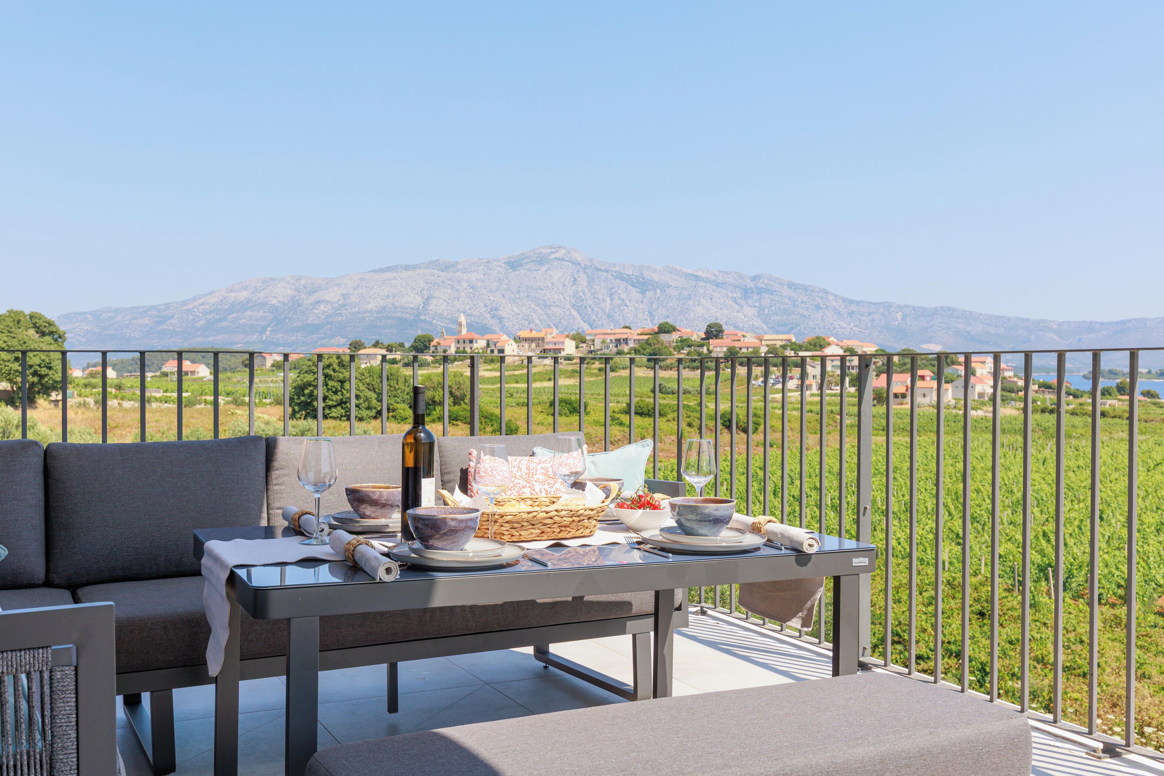 A balcony with a table set for dining, overlooking a mountainous landscape.