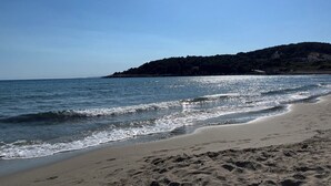 Ein Strand mit blauem Himmel, ruhigem Wasser und einer entfernten Hügelkette mit Gebäuden.