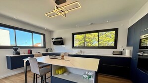 A modern kitchen with a central island, bar stools, a built-in oven, and large windows.