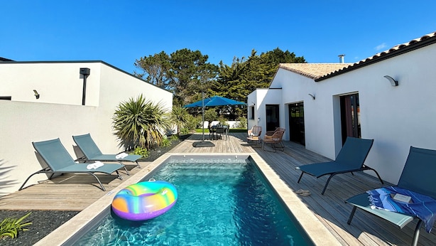 A swimming pool with lounge chairs, a wooden deck, and a blue umbrella.