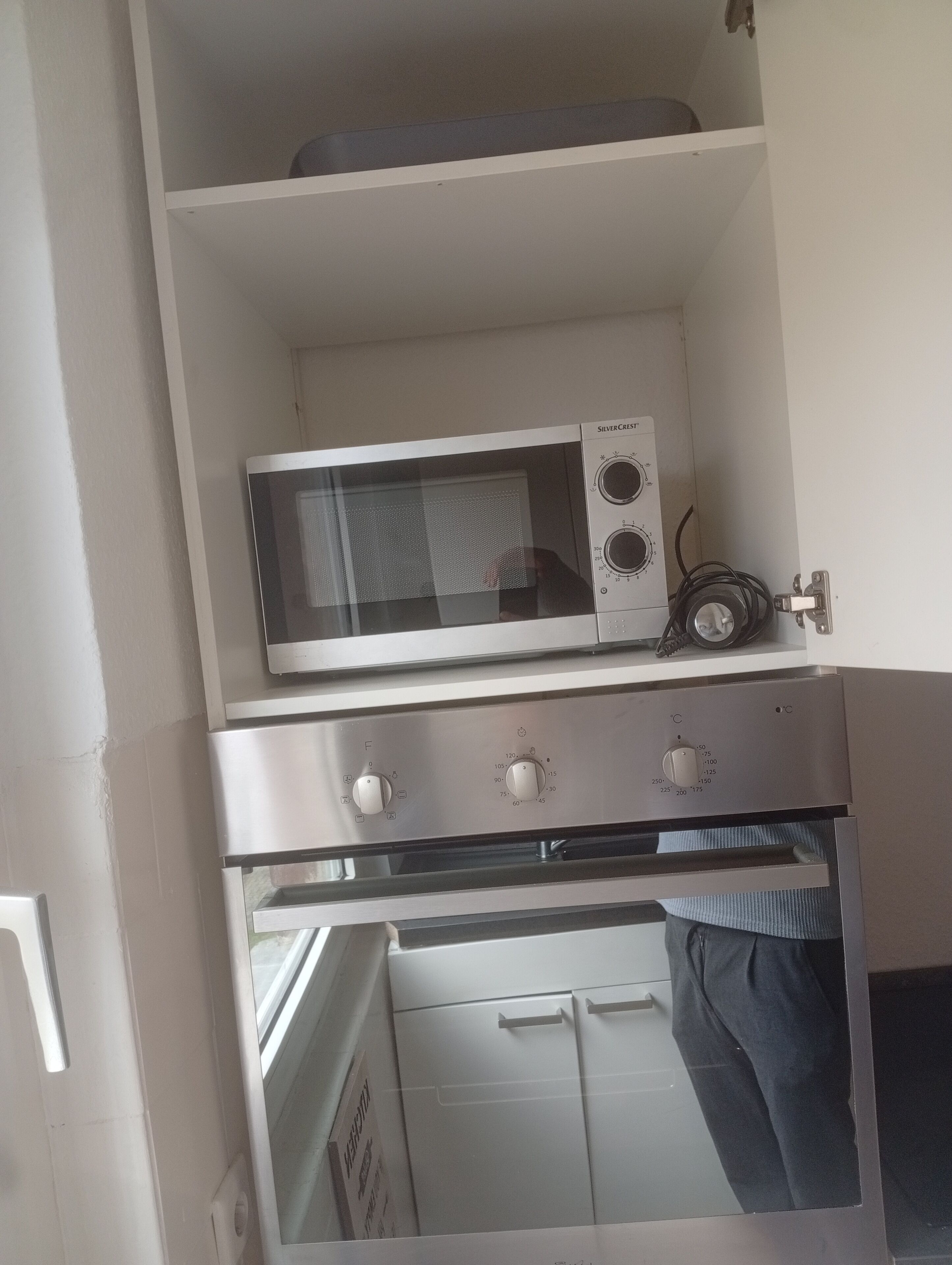 A kitchen with a microwave and oven, a white cabinet, and a window.