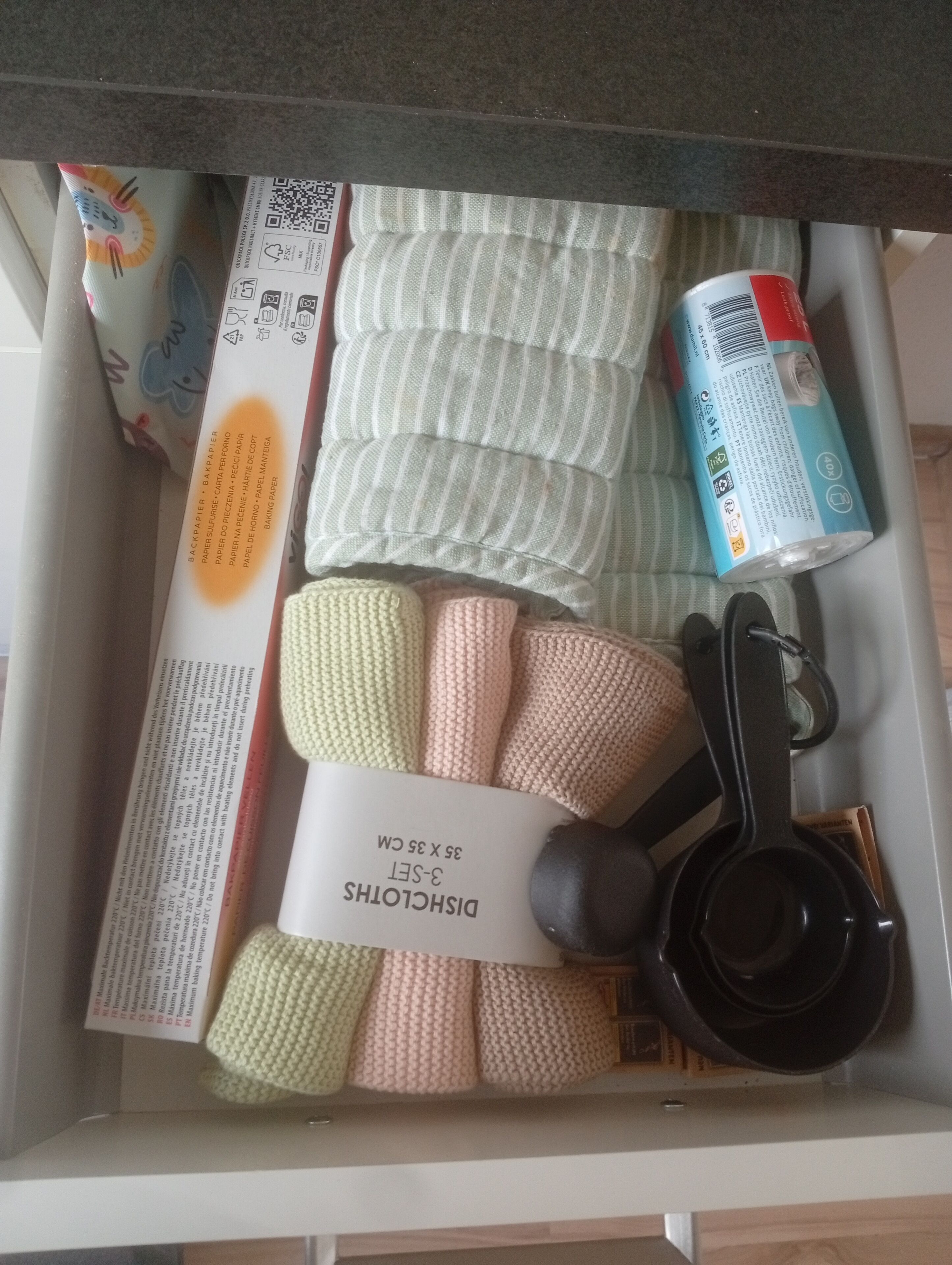 Un cajón con varios objetos, incluyendo una caja de toallas de papel, una lata de refresco y una taza medidora.