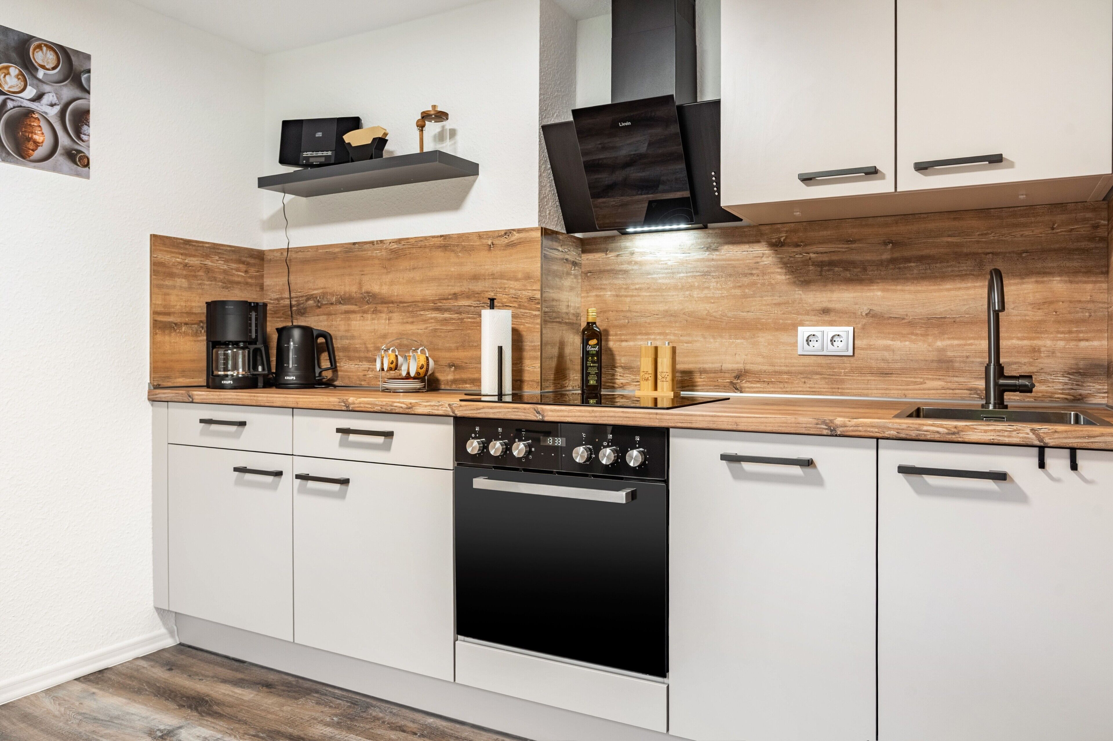 A modern kitchen with white cabinetry, a wooden countertop, a coffee maker, a kettle, and a built-in oven.