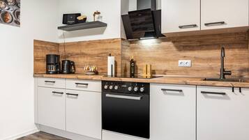 A modern kitchen with white cabinetry, a wooden countertop, a coffee maker, a kettle, and a built-in oven.