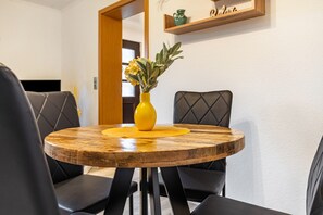 Una mesa redonda de madera con un jarrón amarillo y flores amarillas, rodeada de sillas tapizadas en negro.