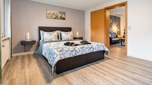 A bedroom with a large bed, bedside lamps, a wooden floor, and a painting on the wall.
