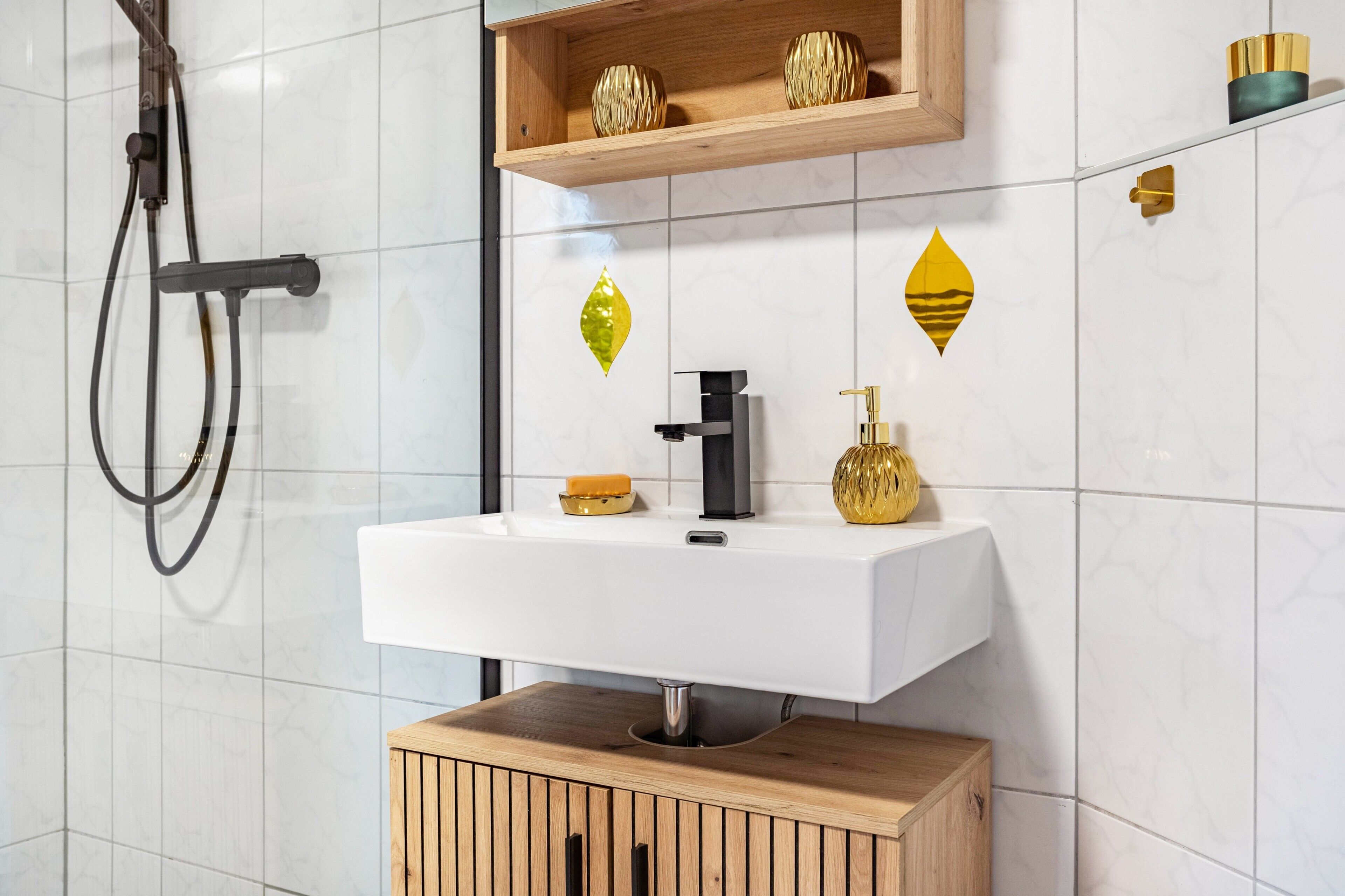 Ein modernes Badezimmer mit einem weißen Waschbecken, einem Holzschrank und dekorativen Wandfliesen.