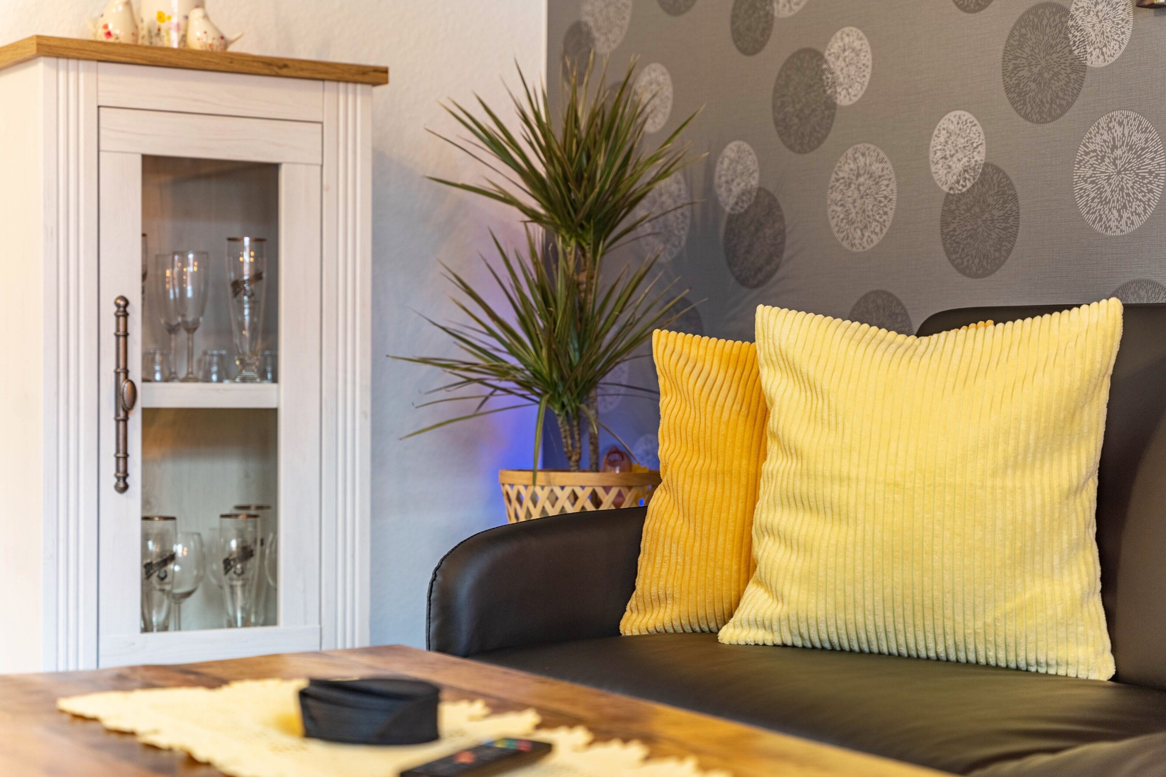 A living room with a sofa, a cabinet with glass doors, and a potted plant.