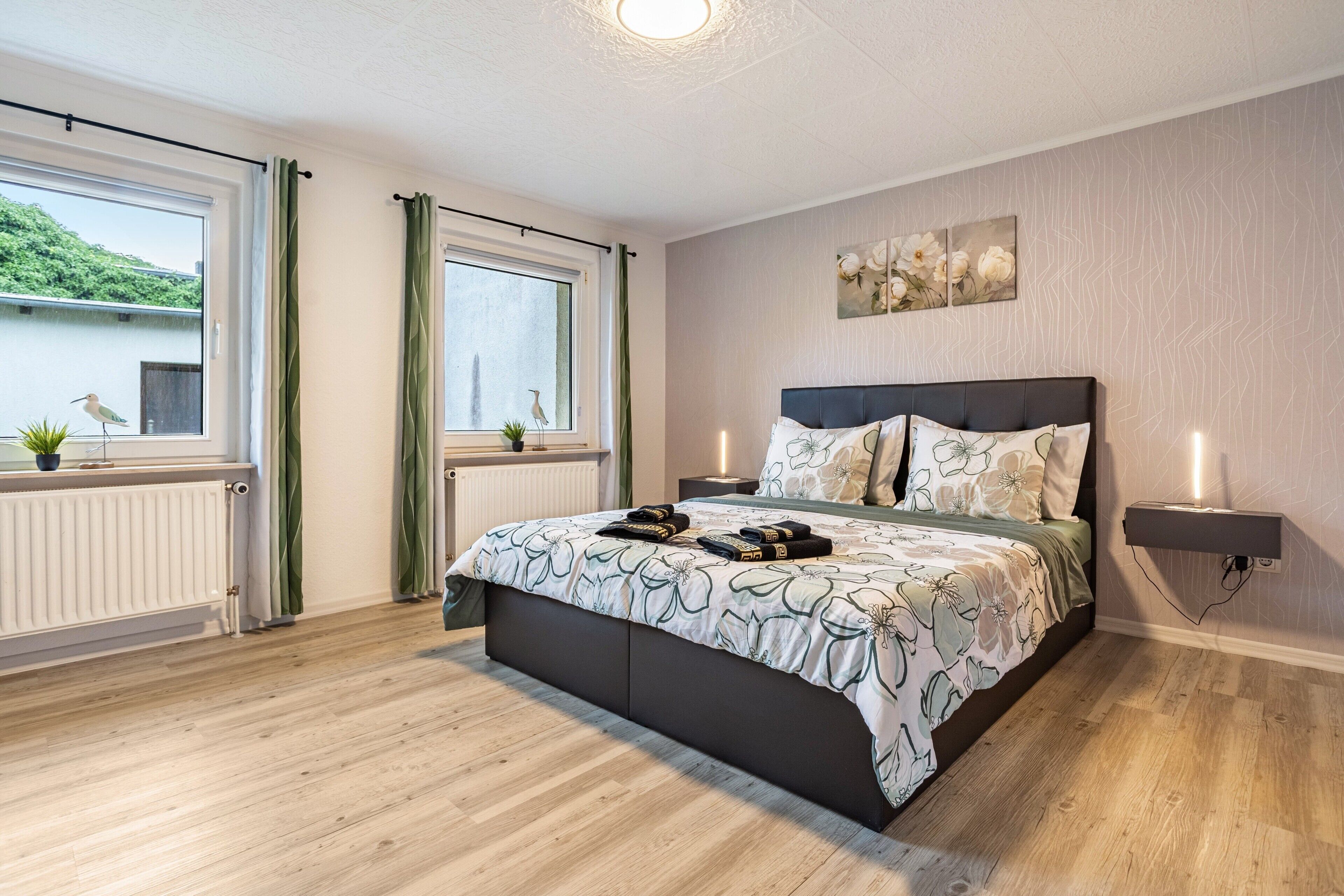 Ein Schlafzimmer mit Bett, Nachttischen, einem Heizkörper und einem Fenster mit Vorhängen.