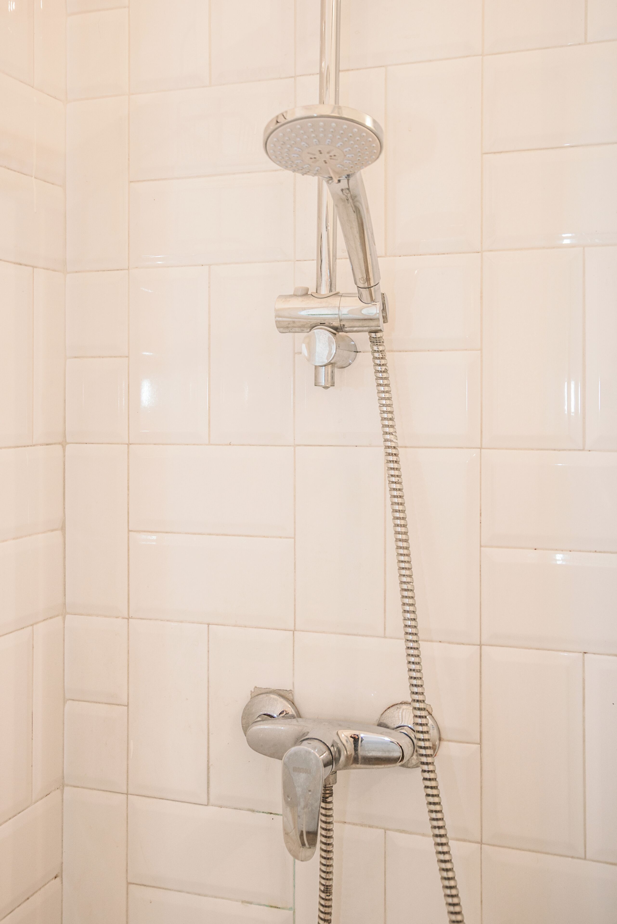 A shower with a handheld showerhead and a fixed wall-mounted showerhead, both with chrome finishes.