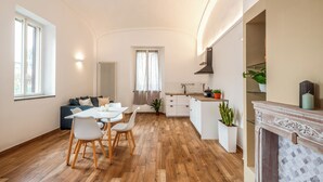 Una cucina moderna con pavimento in legno, una zona pranzo con tavolo e sedie bianche, un'isola integrata con lavello e un caminetto con mensola.