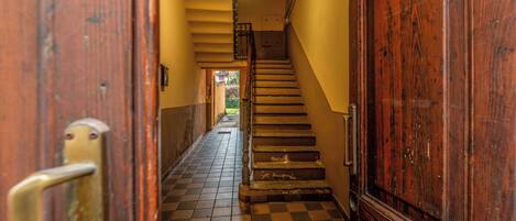 Un couloir doté d’un sol à carreaux, de portes en bois et d’un escalier menant à un étage supérieur.