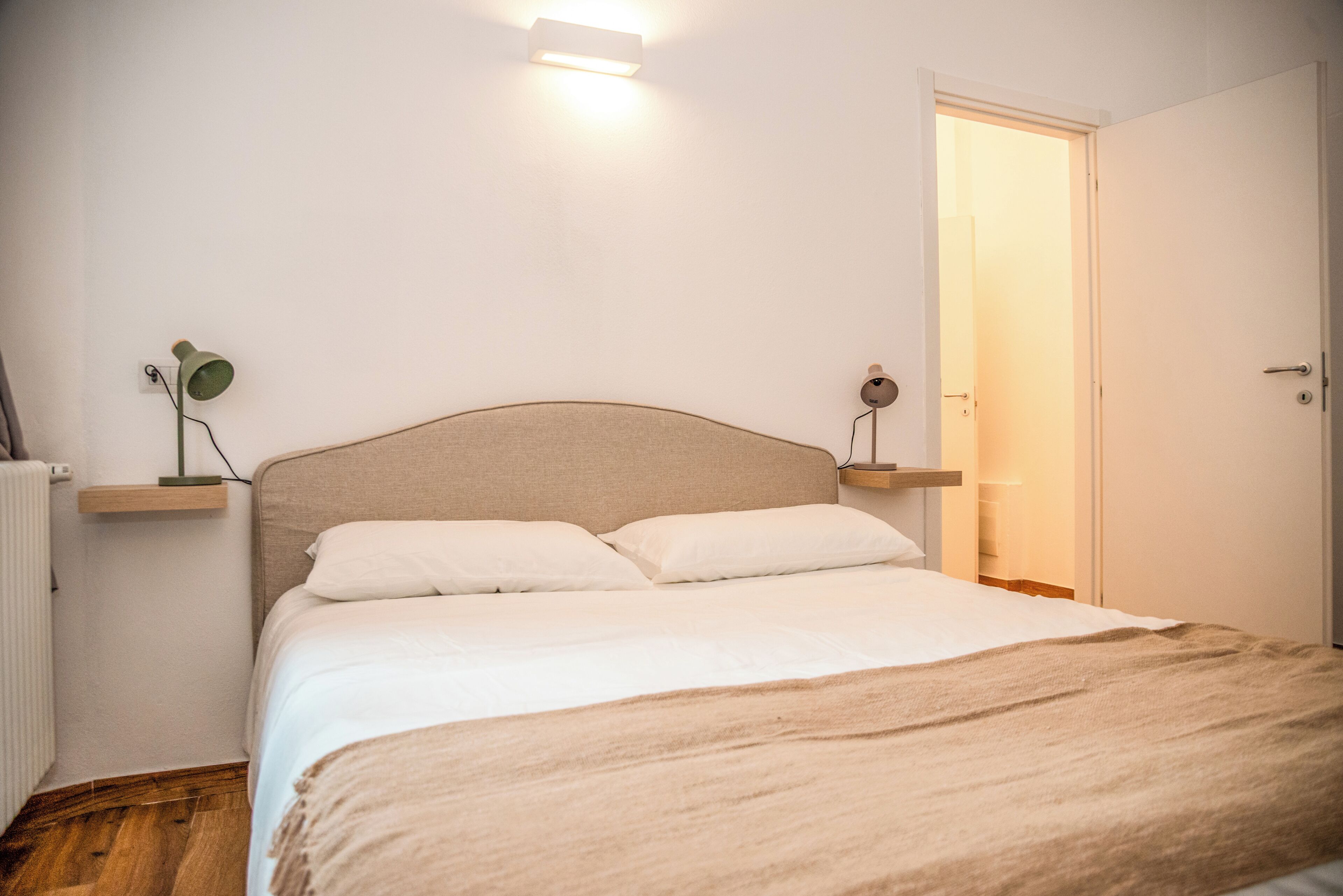 A bedroom with a bed, bedside tables, a radiator, and a door.