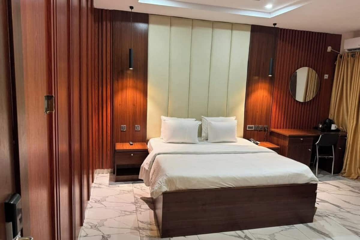 A hotel room with a bed, bedside tables, a desk, and a mirror.