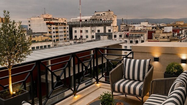 A rooftop terrace with wicker furniture, a round table, and a view of the cityscape.