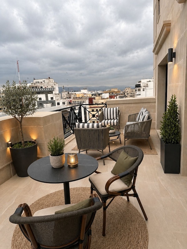 Eine Dachterrasse mit rundem Tisch, Korbstühlen und Blumentöpfen.