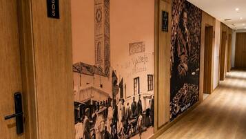 Un pasillo con puertas de madera, un mural en la pared que representa una escena histórica, y un cartel que indica la habitación número 505.