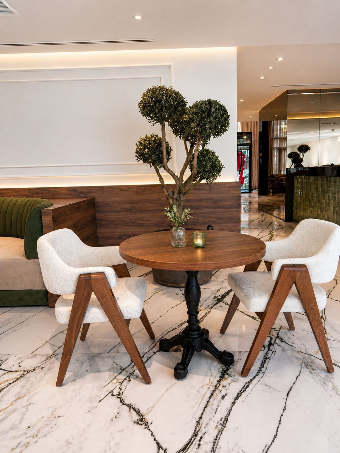 Een ronde houten tafel met twee witte stoelen, een kleine vaas met planten en een marmeren vloer.