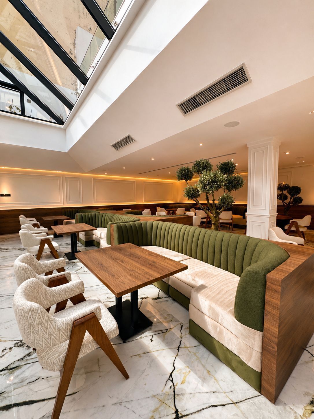 A modern interior with a high ceiling, marble flooring, and a seating area with green upholstered sofas and white armchairs.