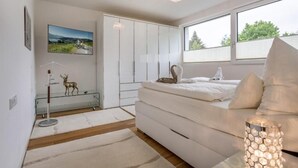 Ein modernes Schlafzimmer mit Bett, einem Glastisch, einer Chandelier und einem Fenster mit Blick.