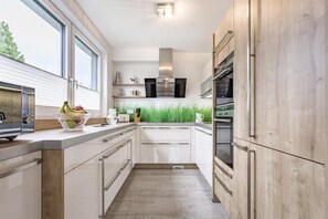 A modern kitchen with white cabinetry, a wooden countertop, and a view of the outdoors through large windows. - Luxury Apartment Silvia by we rent (Zell am See)