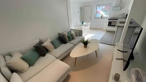 Moderni olohuone, jossa on sohva, sohvapöytä ja televisio. Taustalla näkyy keittiö.
