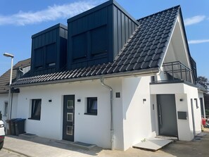 Een modern gebouw met twee verdiepingen, een donker dak, witte muren en een kleine veranda.