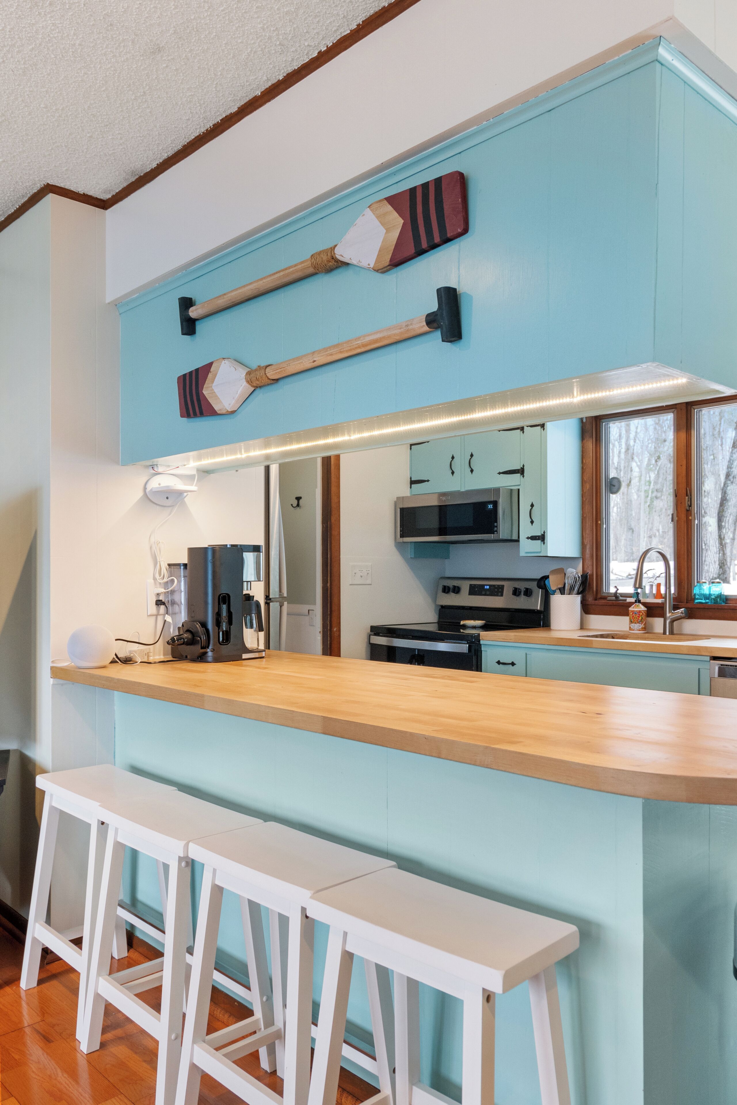 A kitchen with a wooden countertop, white bar stools, a microwave, and a stove.